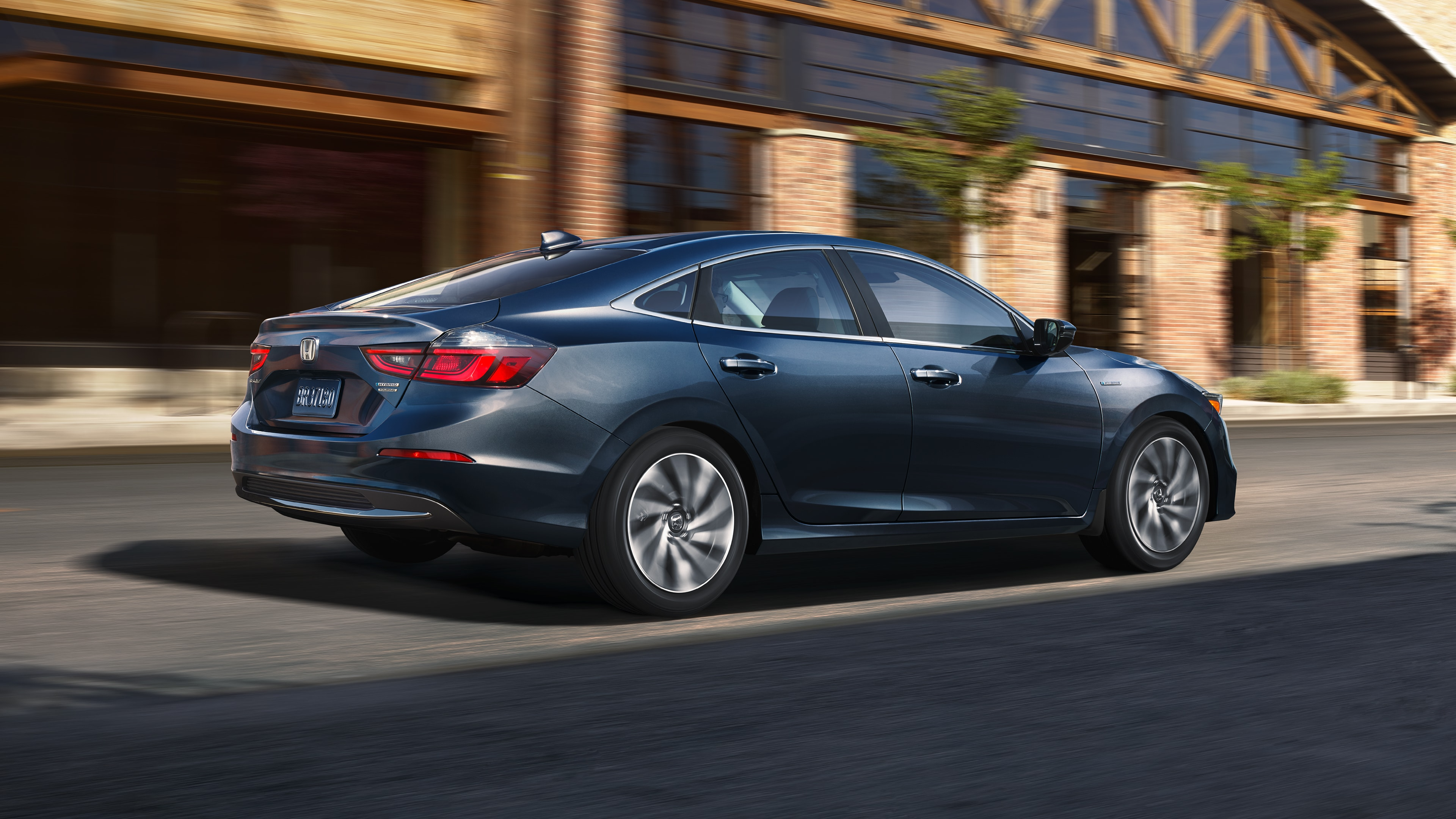 Rear side view of Honda Insight driving in front of a brick building