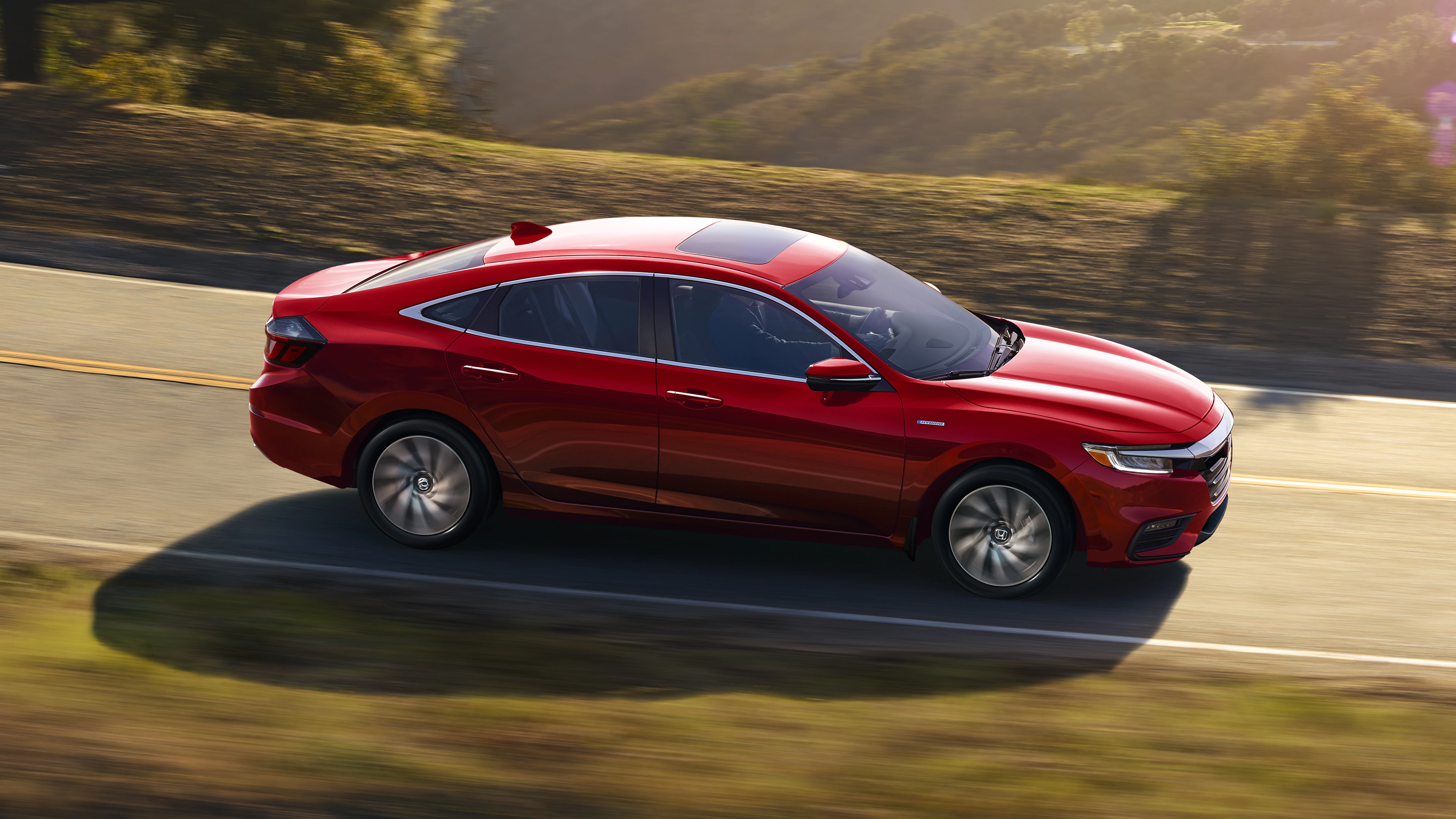 Side view of Honda Insight driving in the country with a valley behind it filled with trees